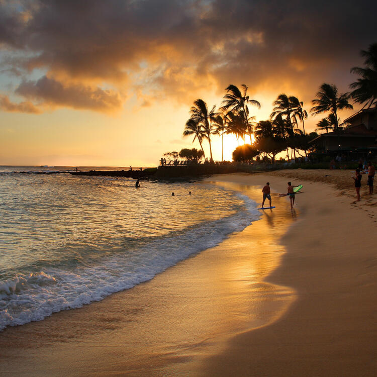 Malerischer Sonnenuntergang am Poipu Beach auf Kauaʻi, Hawaii, mit Menschen, die am Strand spazieren und das warme Licht genießen