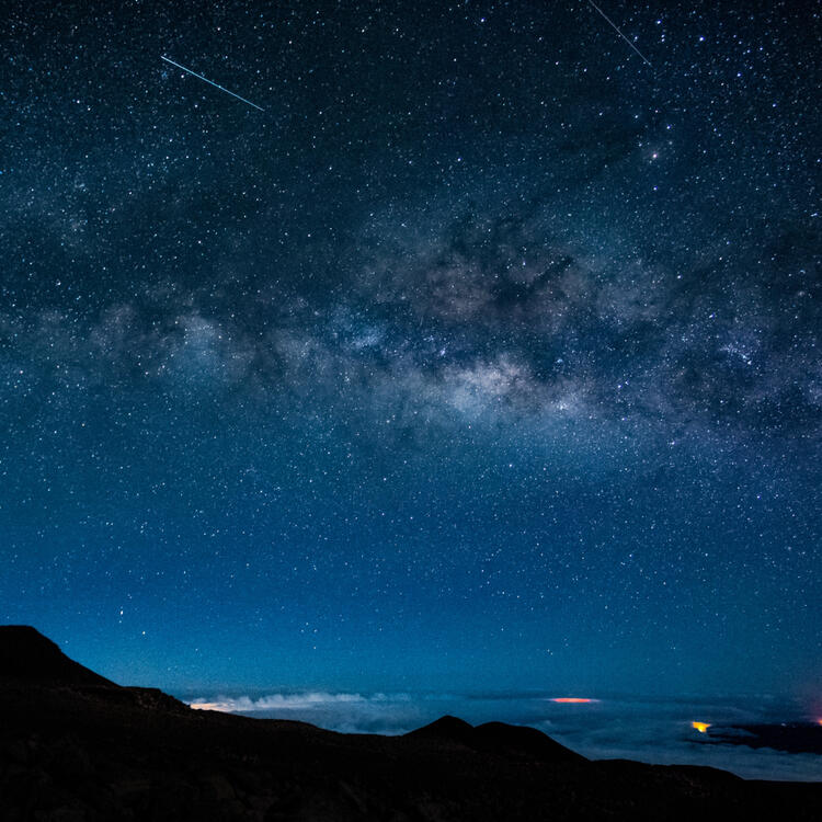 Spektakulärer Nachthimmel über Hawaii mit sichtbarer Milchstraße und Sternschnuppen, über einem dunklen, bergigen Horizont