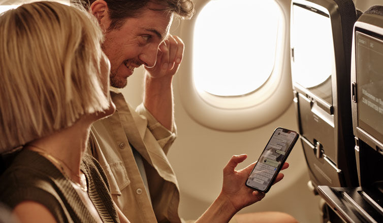 Ein Paar sitzt im Flugzeug und schaut sich gemeinsam Nachrichten auf dem Handy an