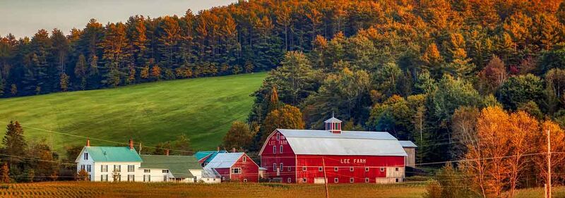 Mehrere rote Farmgebäude in New Hampshire vor bunt gefärbtem Wald