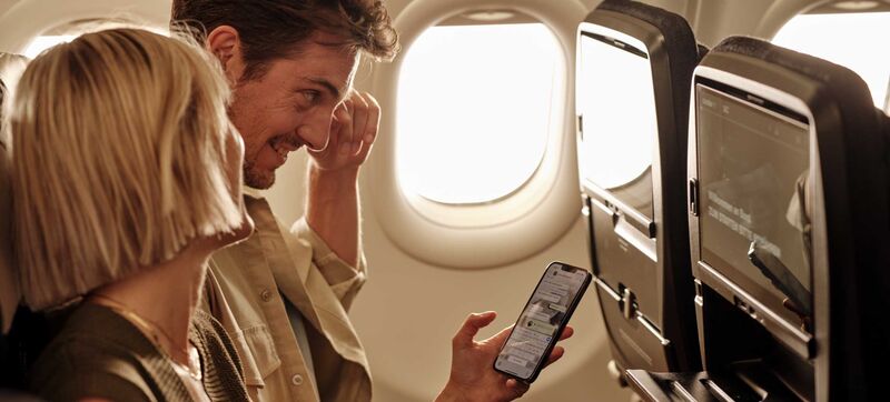 Ein Paar sitzt an Bord eines Flugzeugs und liest gemeinsam auf dem Smartphone Chatnachrichten
