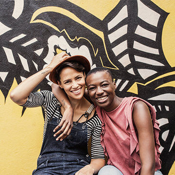 Couple in front of a vibrant yellow mural with black leaf patterns, sharing a joyful moment.