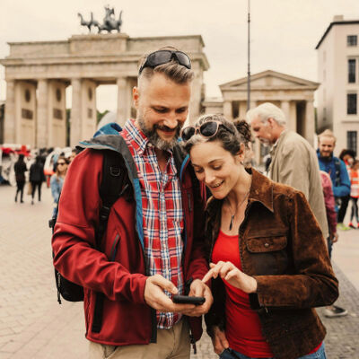 Happy couple looking at a smartphone together in front of the Brandenburg Gate with tourists in the backgroun