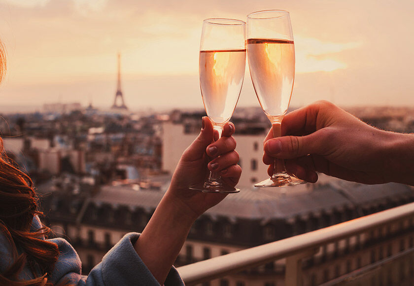 Two people toasting with champagne against a panoramic backdrop of Paris, featuring the Eiffel Tower.