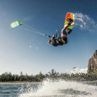 Kite surfer performing a high jump over the water with a clear blue sky and coastline in the background