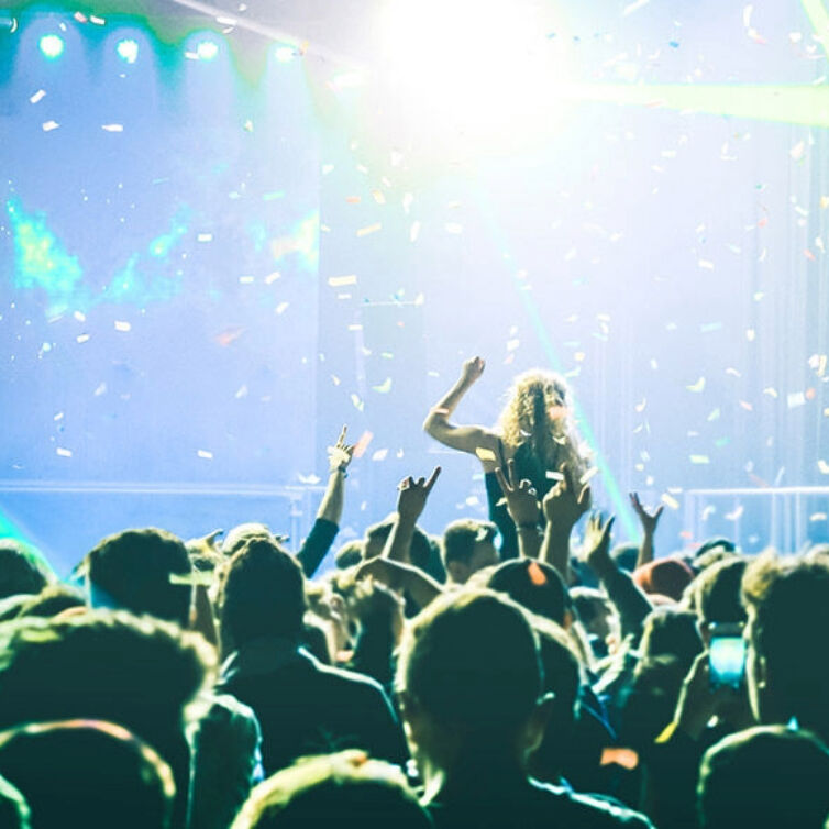 Crowd at a music festival, illuminated by bright stage lights with hands raised in celebration
