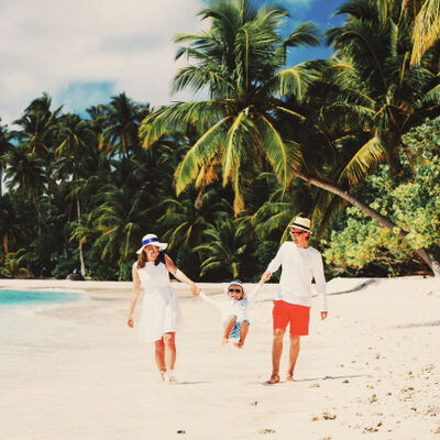 A family of three, walking hand in hand on a tropical beach with palm trees in the background