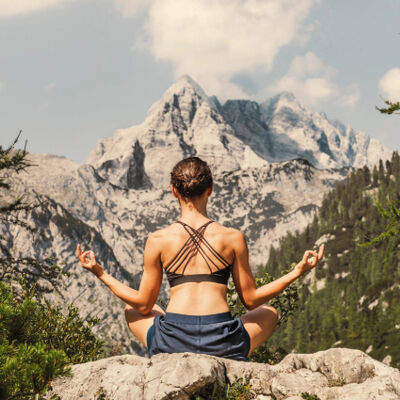 Woman in a yoga pose meditating on a rock with a majestic mountain range in the background
