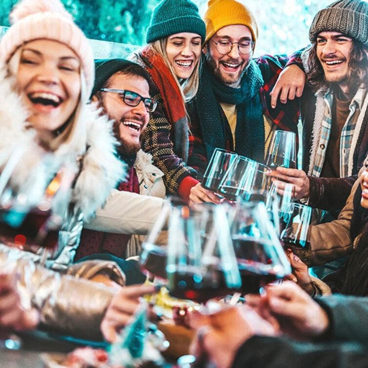  A joyful group of friends dressed in winter clothing, toasting with glasses of red wine, sharing a festive moment