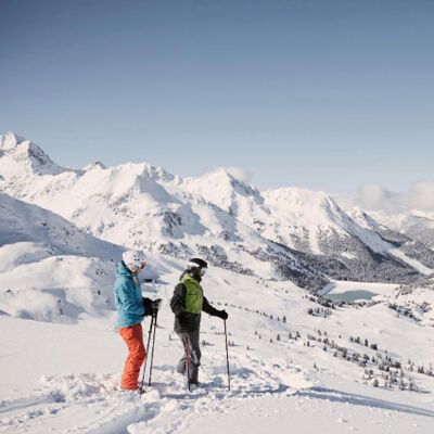 Two skiers standing on a snowy mountain slope with scenic alpine peaks in the background