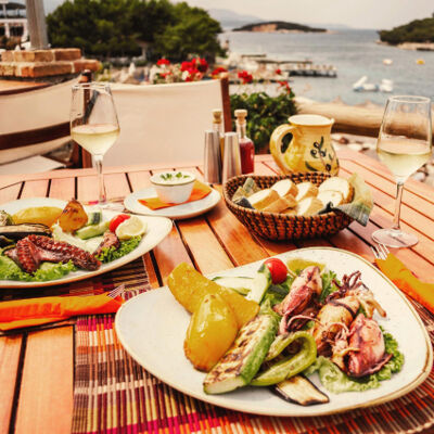Gourmet seafood meal with a glass of white wine at an outdoor seaside restaurant with a view of the harbor