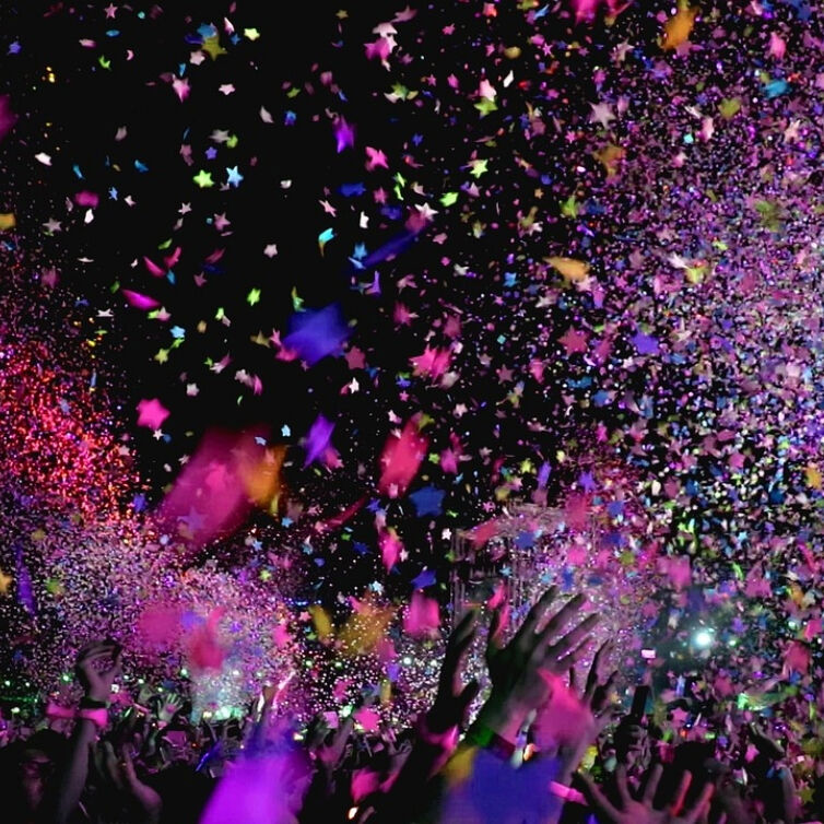 A vibrant explosion of colorful confetti raining down on an exuberant festival crowd with hands reaching towards the sky