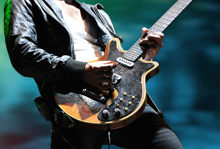 A close-up shot of a person playing an electric guitar, focusing on the hands and the guitar body with a blurred background.