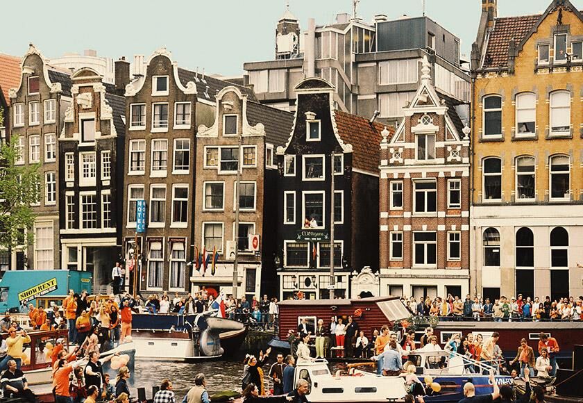 Canals of Amsterdam with colorful historic buildings, a prominent monument, and vibrant activity.