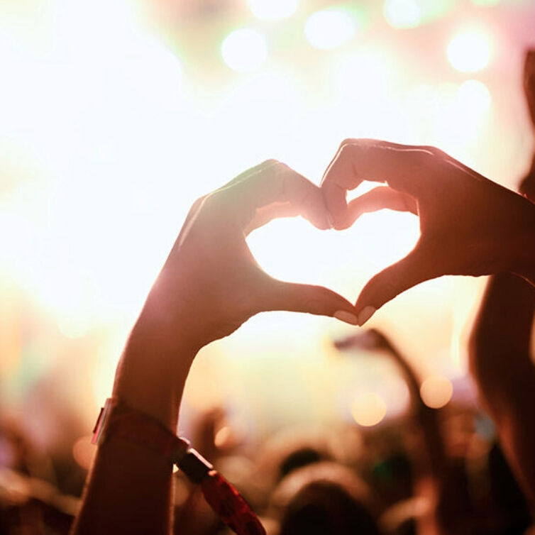 Hands forming a heart shape against a backdrop of warm stage lights, capturing a moment of love and connection at a festival