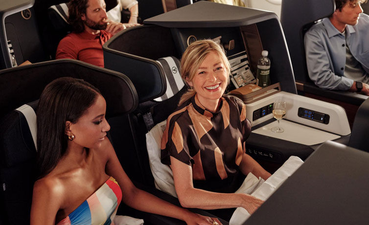 Two women on bord a plane are enjoying business class seats