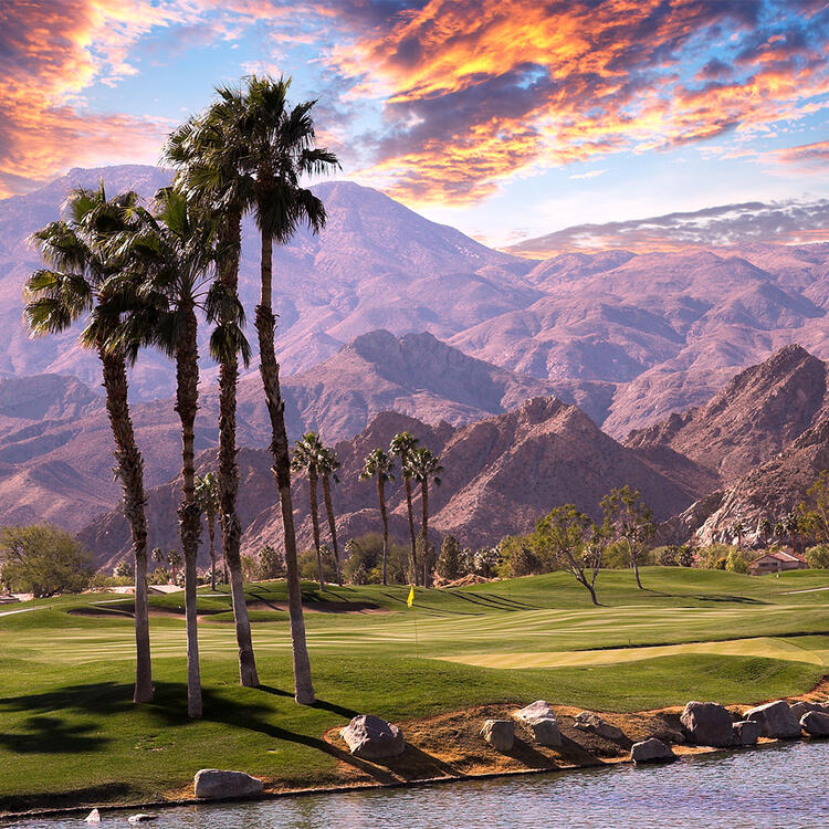 Ein Golfplatz bei Sonnenuntergang in Palm Springs, Kalifornien, mit grünen Fairways und einer Reihe von Palmen.