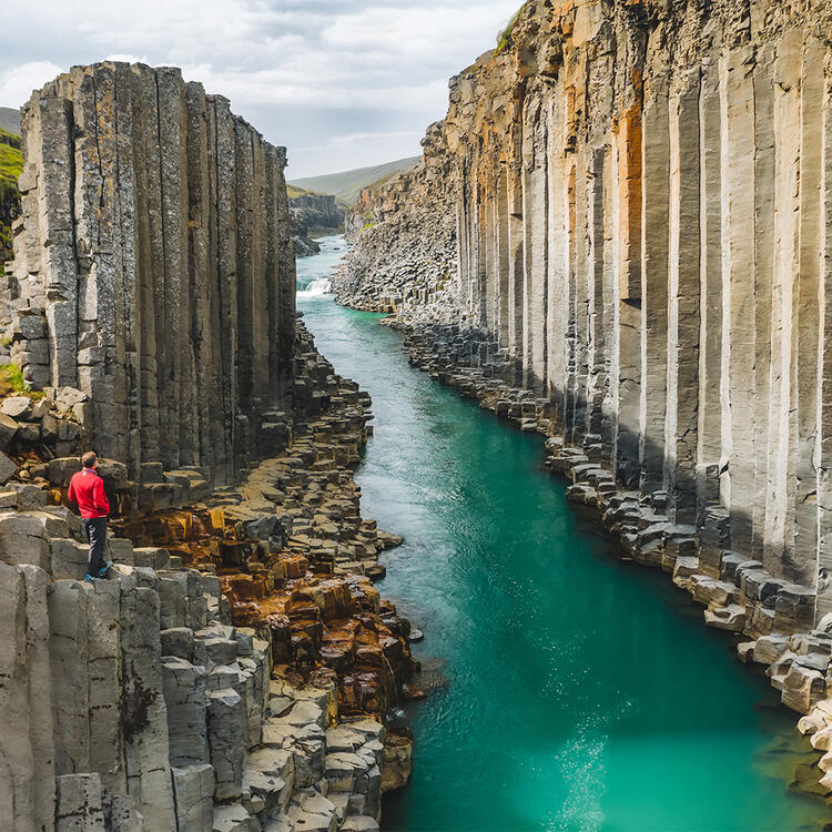 Wanderer in roter Jacke besucht den Basalt-Canyon Stuðlagil mit seltenen vulkanischen Basaltsäulenformationen in Island