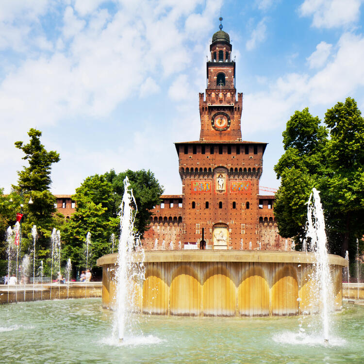 Frontansicht der Burg mit einem prunkvollen Brunnen an einem sonnigen Tag