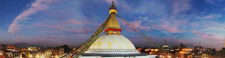 Bodhnath Stupa in Kathmandu bei Sonnenuntergang, umgeben von Gebetsfahnen und bunten Gebäuden.