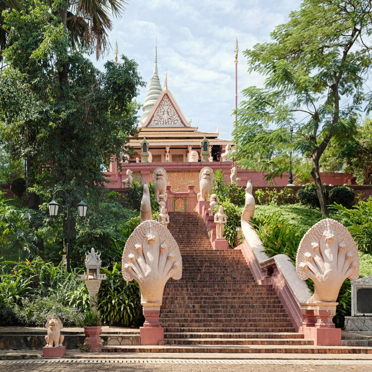 Zentraler Aufgang zum Wat Phnom mit Naga-Balustraden und Tempelspitze hinter grünen Bäumen sichtbar.