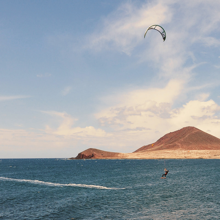 Mann Kitesurfen an der Küste in der südlichen Teneriffa mit Blick auf das lokale Wahrzeichen Montaña Roja.