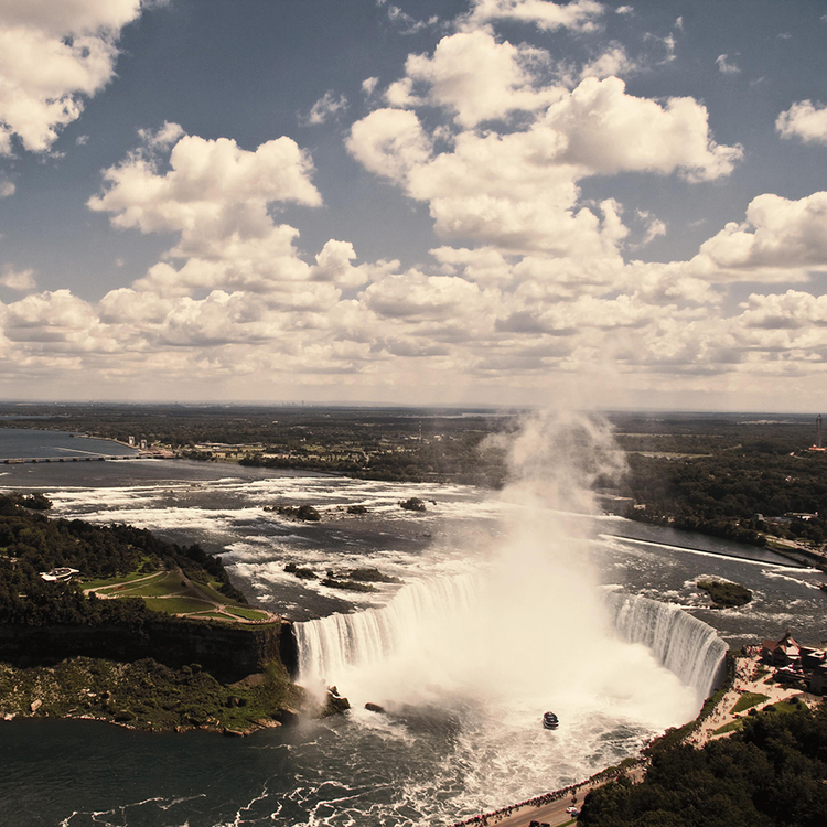 Luftaufnahme der Niagarafälle auf der kanadischen Seite. Die Fälle sind beeindruckend und majestätisch, das Wasser fällt in eine tiefe Schlucht hinab. 