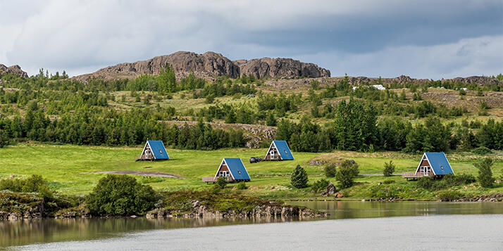 Egilsstadir, Island - Gemütliche Hütten mit traditioneller Architektur und blauen Dächern entlang des Flusses und der Ringstraße.