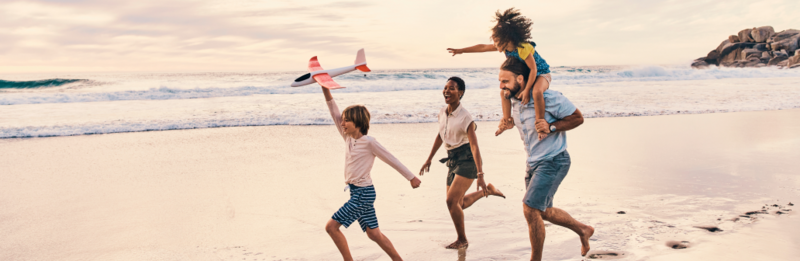 Eine vierköpfige Familie rennt lachend über einen Sandstrand