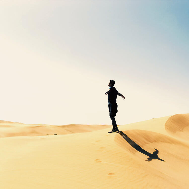 Mann, der mit ausgestreckten Armen auf einer Sanddüne am Strand steht, Fuerteventura, Kanarische Inseln, Spanien