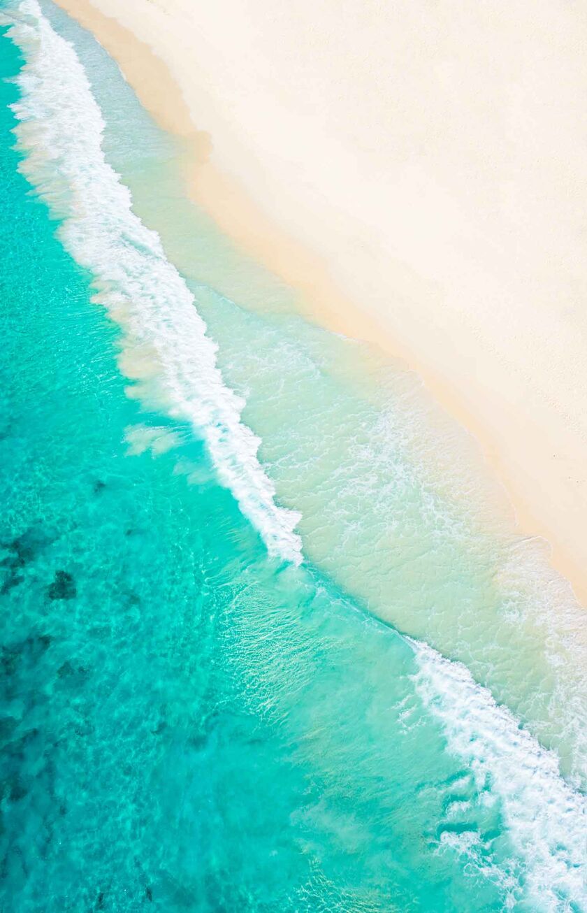Ein Bild aus der Vogelperspektive von türkisblauem Meer und weißem Sandstrand