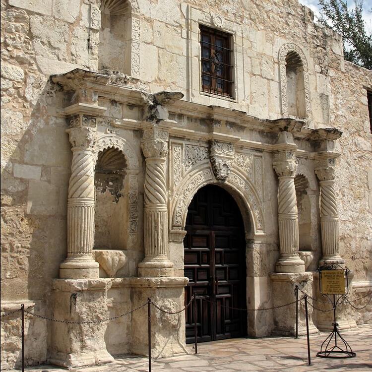 Die historische Fassade des Alamo-Missionsgebäudes in San Antonio, Texas, mit kunstvoll verzierten Säulen, Bögen und einer schweren Holztür.