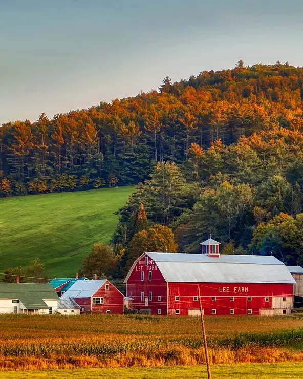 A red barn in the field in New Hampshire, trees with colorful leaves in the background