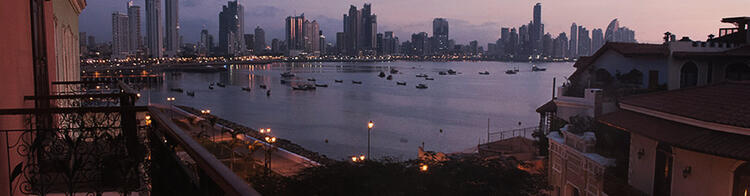 Večerní pohled z balkonu na panorama Panama City s osvětleným pobřežím a loděmi v zátoce.