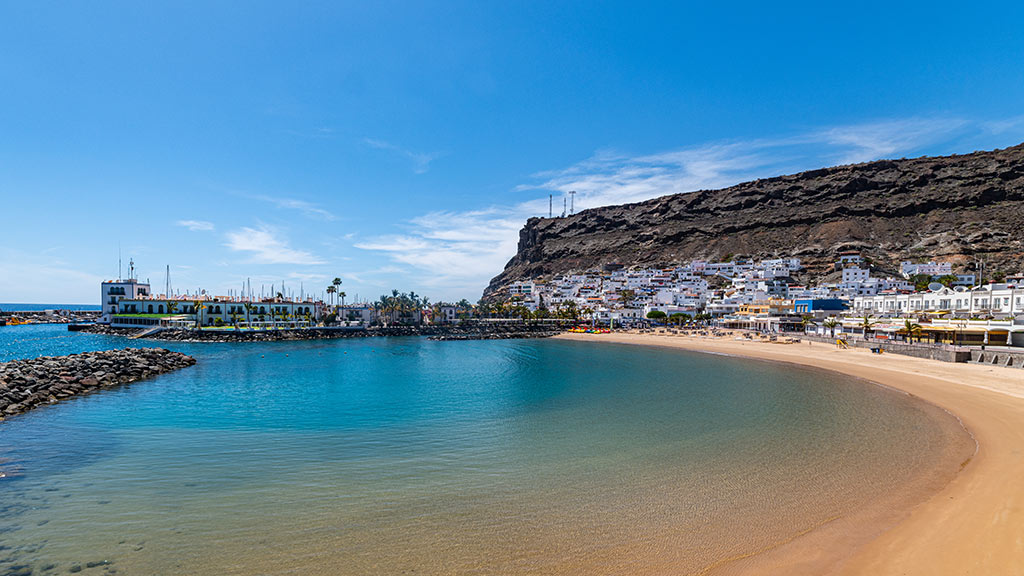 Blick auf Bucht von Puerto de Mogan mit Strand und Häusern im Hintergrund