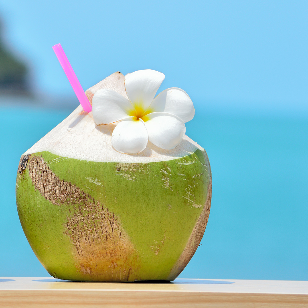 Kokosnuss mit Strohhalm und Blüte steht auf Tisch
