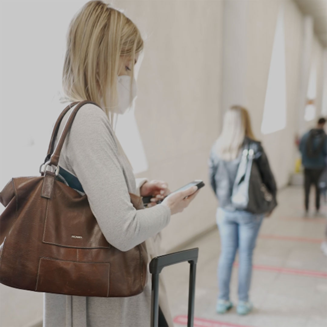 Frau mit Maske und Smartphone in der Hand wartet in einer Schlange am Flughafen