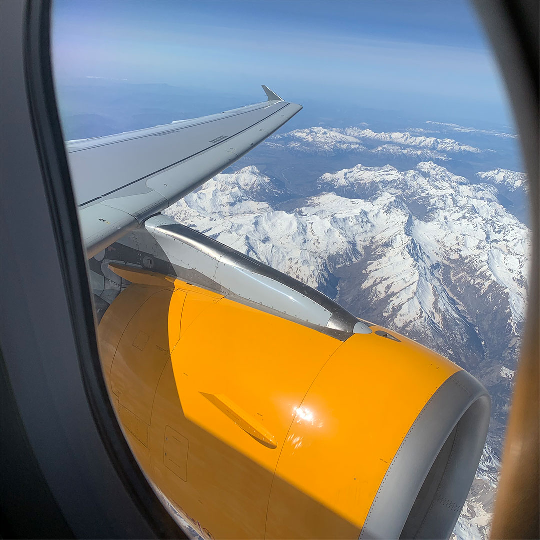 Blick aus Flugzeugfenster mit Tragfläche und schneebedeckten Bergen