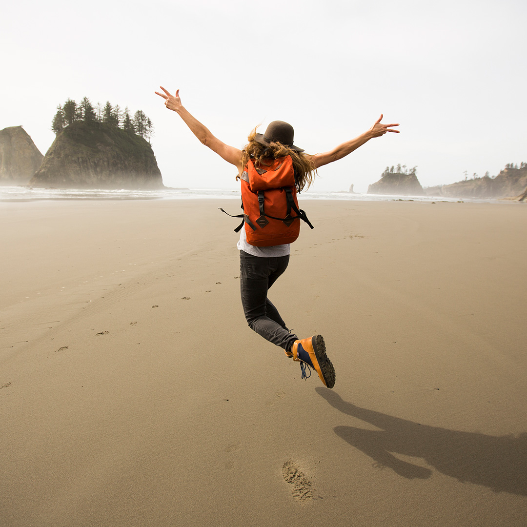 Frau mit Rucksack macht Luftsprung an Strand