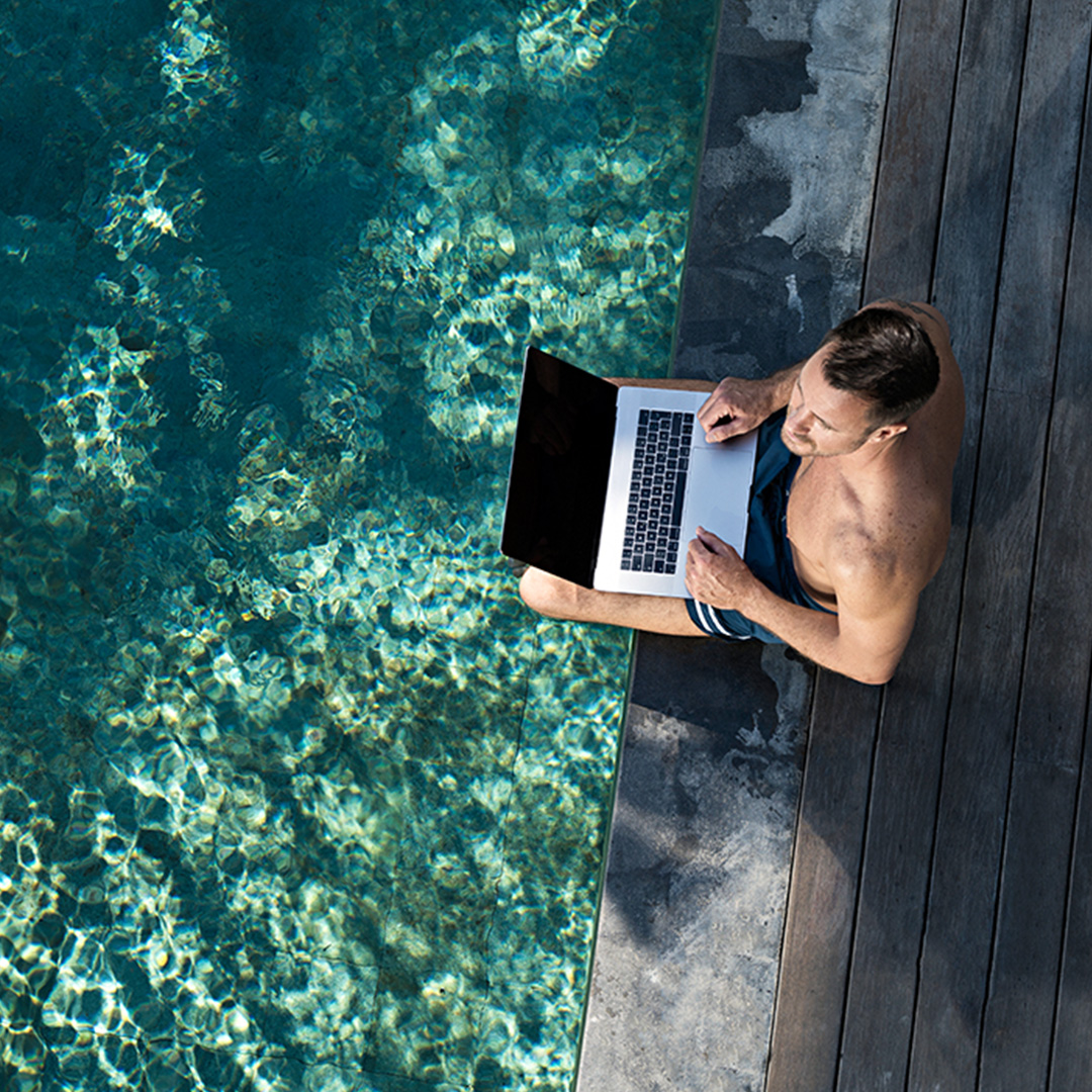Mann mit Laptop sitzt an Pool
