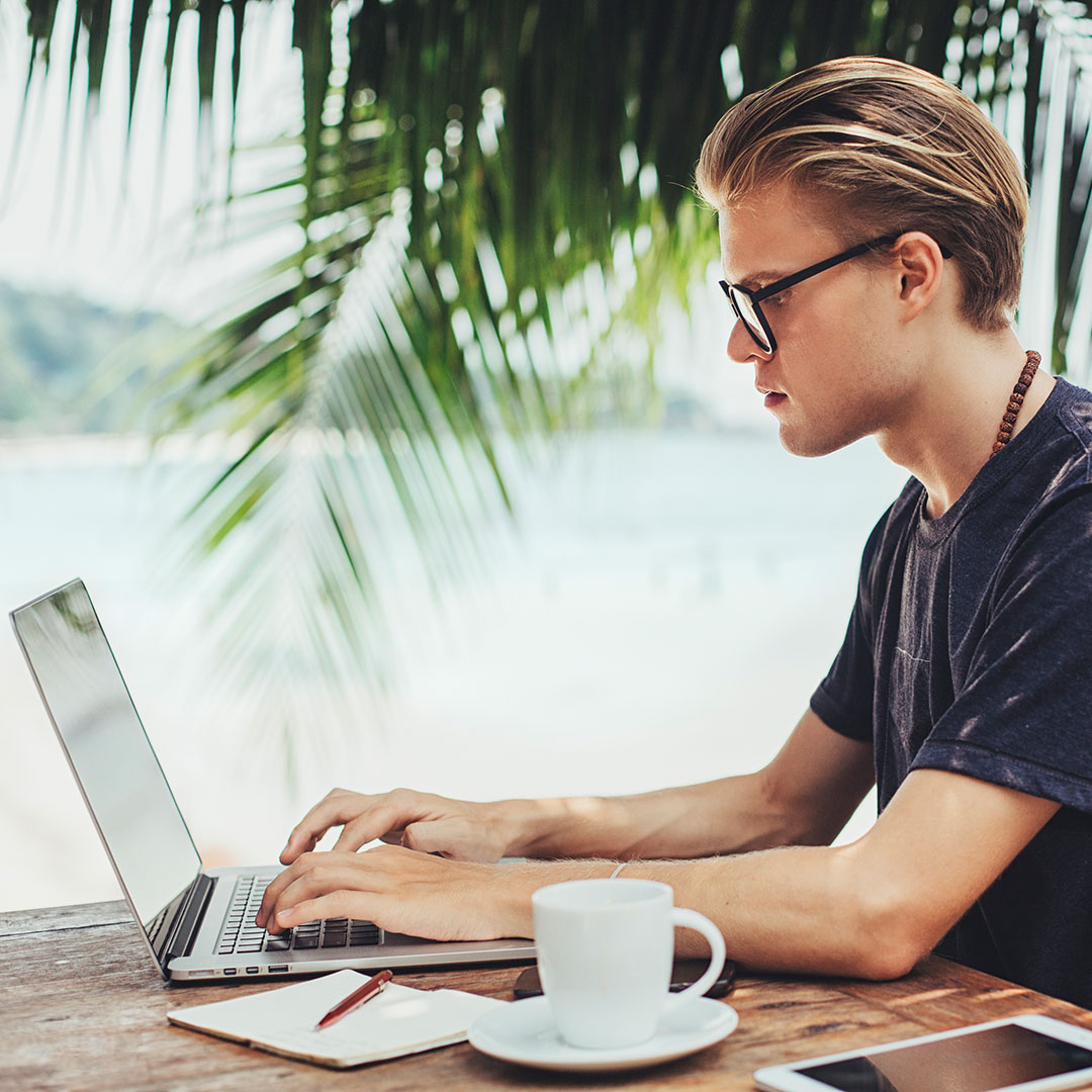 Mann sitzt vor Laptop mit Palmen im Hintergrund