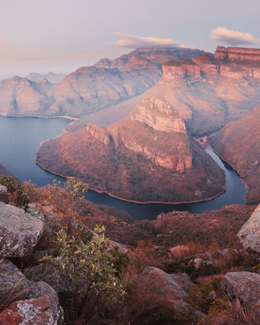 Panoramablick auf den Blyde River Canyon mit Flusskurven und rötlich leuchtenden Felsen bei Sonnenaufgang.