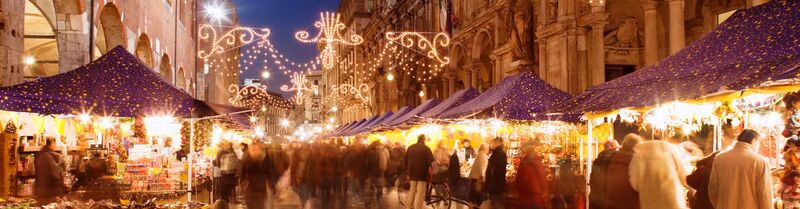 Weihnachtsmarkt in Mailand auf der Piazza del Duomo bei Abenddämmerung, festlich beleuchtete Stände mit blauen Dächern, Lichterketten und Besuchern im warmen Glanz der Weihnachtsbeleuchtung