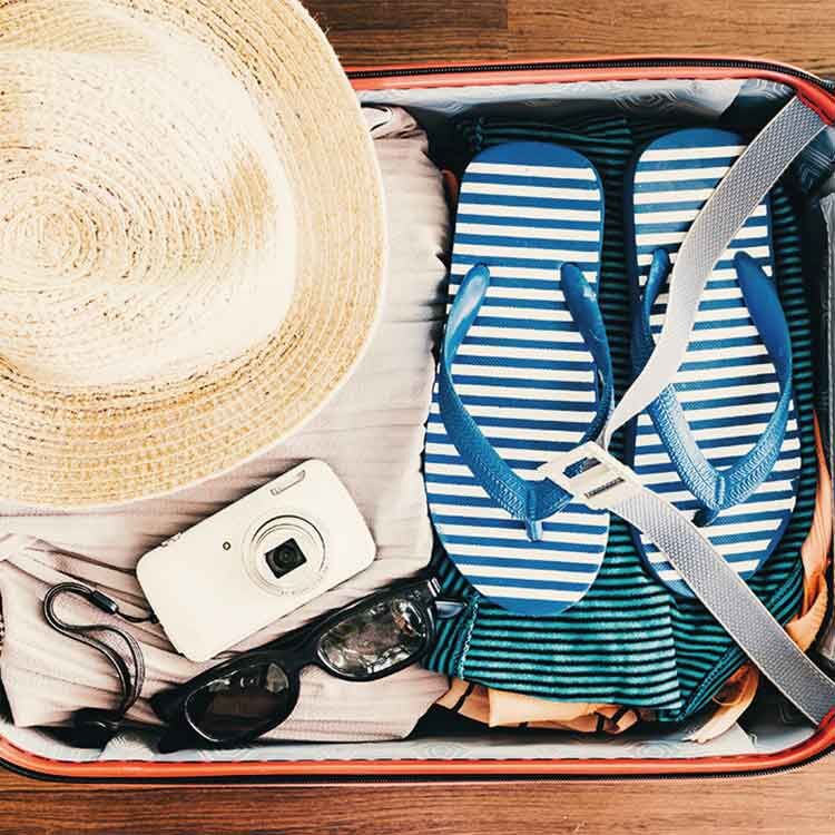 Ein gepackter Koffer mit einem Strohhut, Flipflops und einer kleinen Kamera