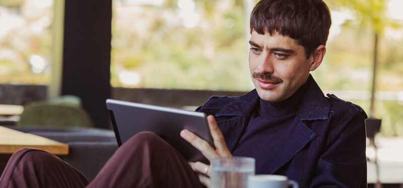 Ein Mann liest ein eJournal auf seinem Tablet, während er einen Kaffee genießt