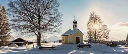 Eine winterlich verschneite Kapelle vor blauem Himmel