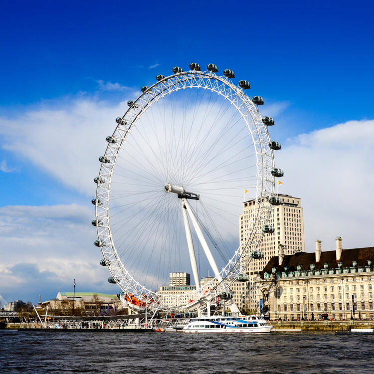 Blick auf das London Eye in London mit der Themse und Gebäuden im Hintergrund.