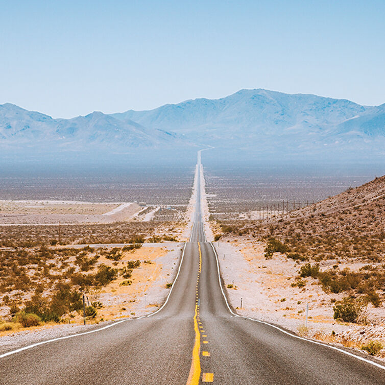Ein Highway führt geradeaus auf eine Bergkette in der Wüste zu