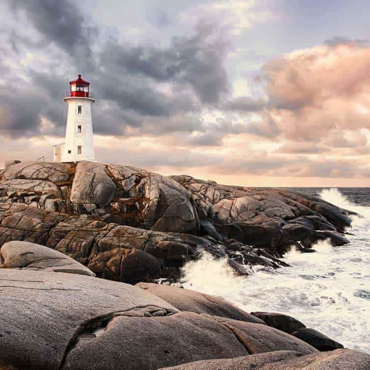 Ein Leuchtturm an der Küste Kanadas, im Vordergrund Felsen und die Brandung