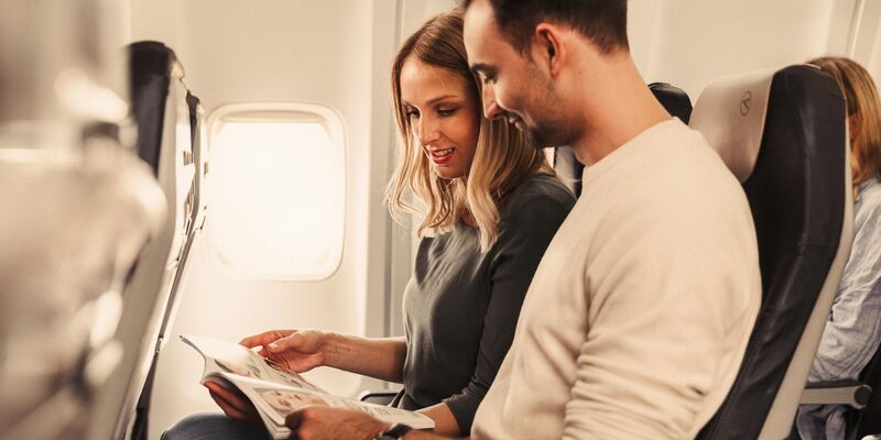 Condor Economy Class Ein Mann und eine Frau lesen gemeinsam ein Magazin im Flugzeug.